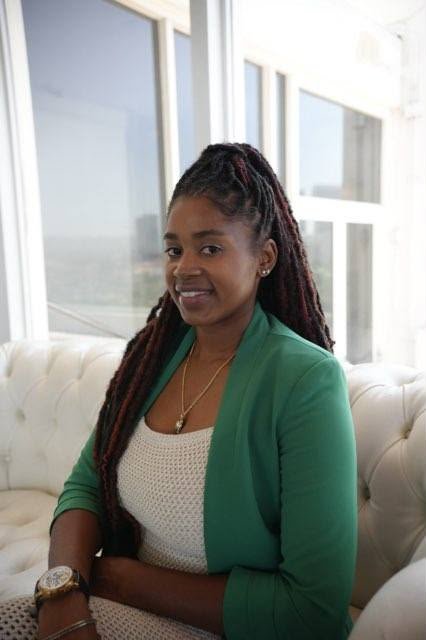 Lovett Love, accountant, smiling in a green blazer on a white sofa by tall windows