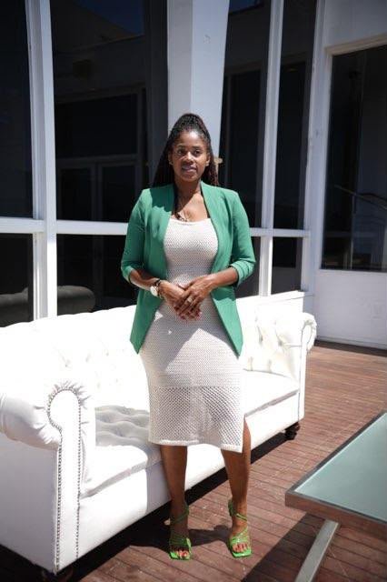 Lovett Love standing on a sunlit deck in a green blazer and white knit dress
